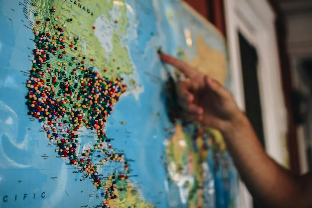 Una mano señala un destino en un mapa lleno de chinchetas